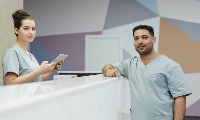 two people in scrubs at a reception desk in a clinic